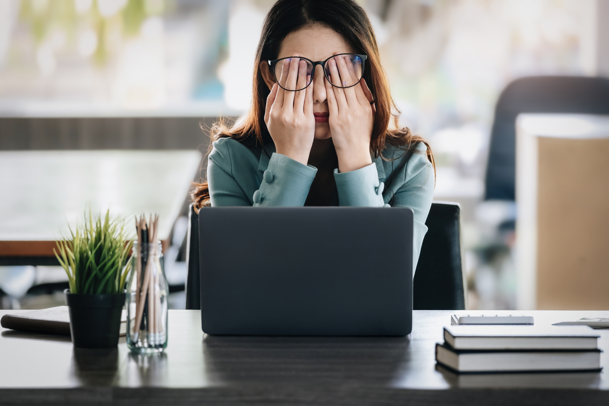 Frustrated employee rubbing her eyes in front of a computer