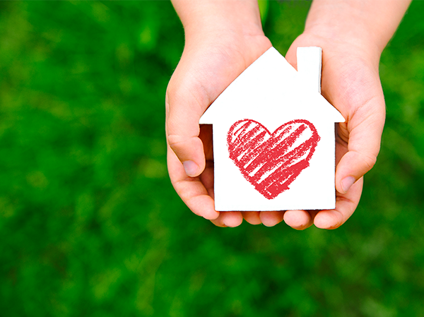 Hands holding a house cut-out with a heart drawn in the center.